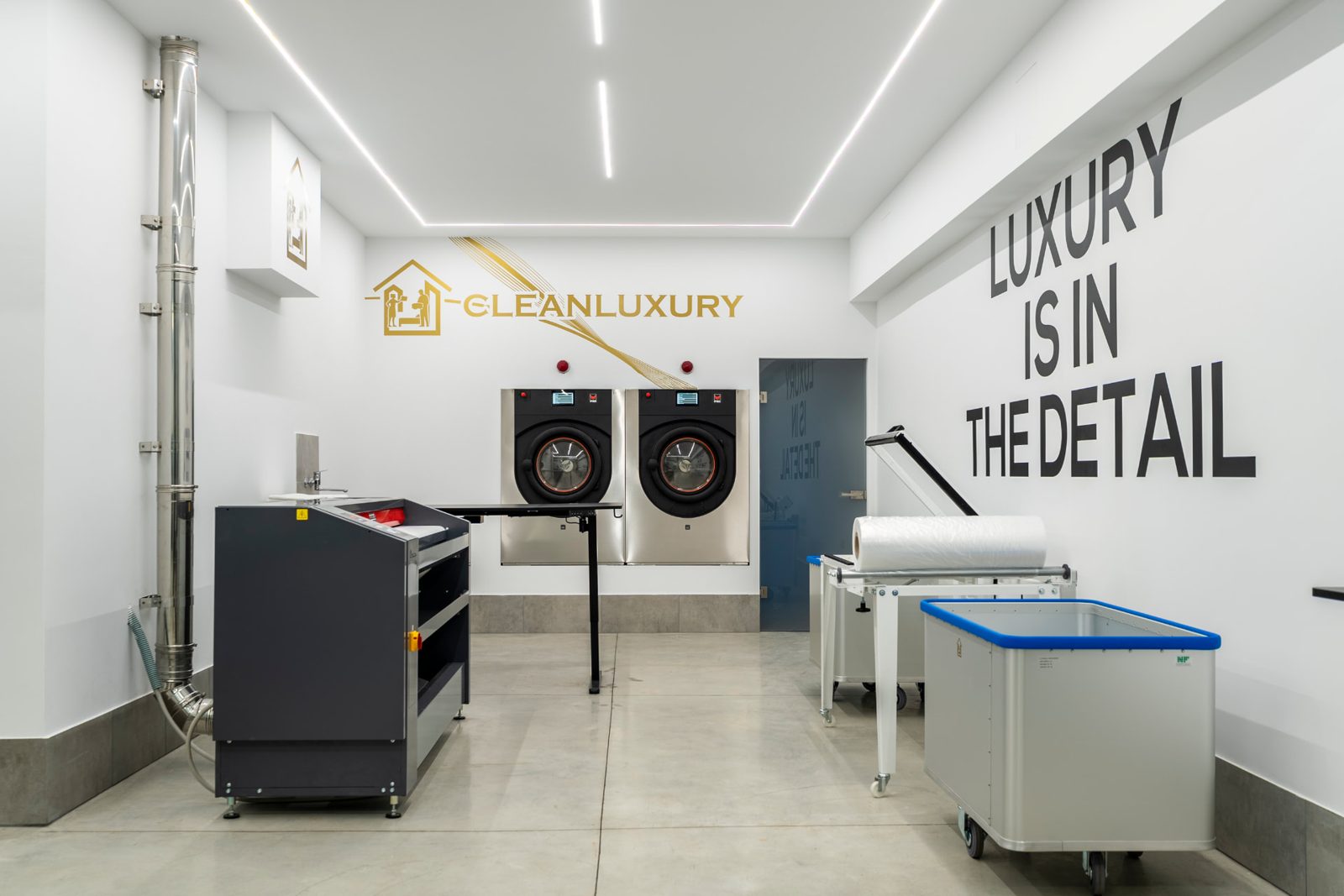Interno di una lavanderia industriale con lavatrici professionali e carrelli di biancheria bianca (immagine illustrativa)