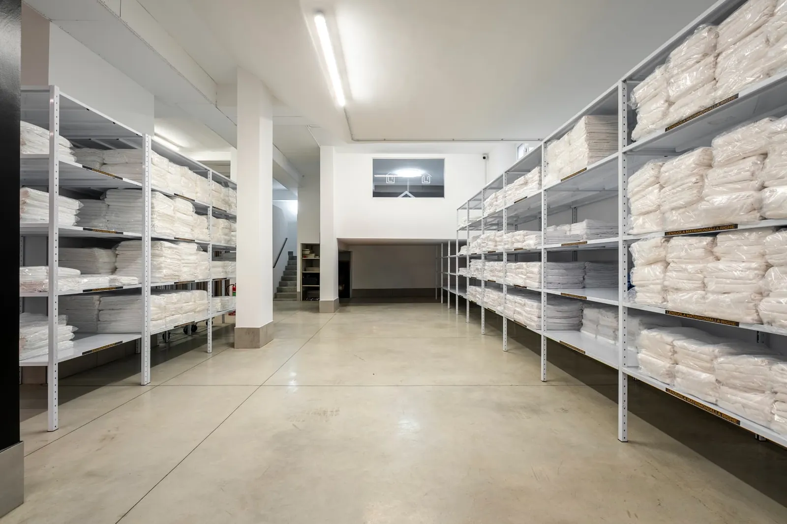 Scaffalature con biancheria bianca piegata e confezionata nel magazzino di Clean Luxury Group